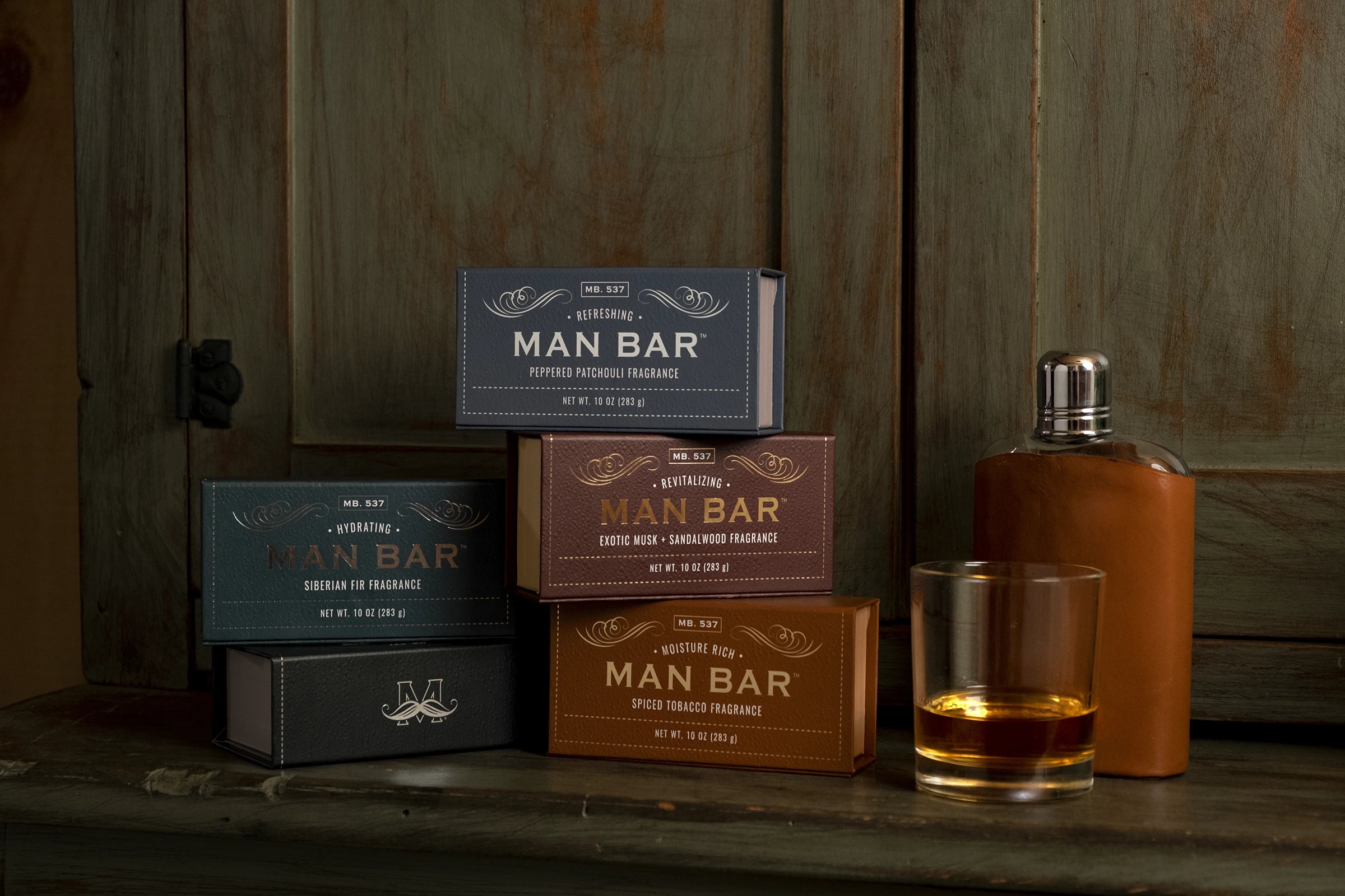 Assortment of Man Bar soap boxes with a whiskey glass and leather flask