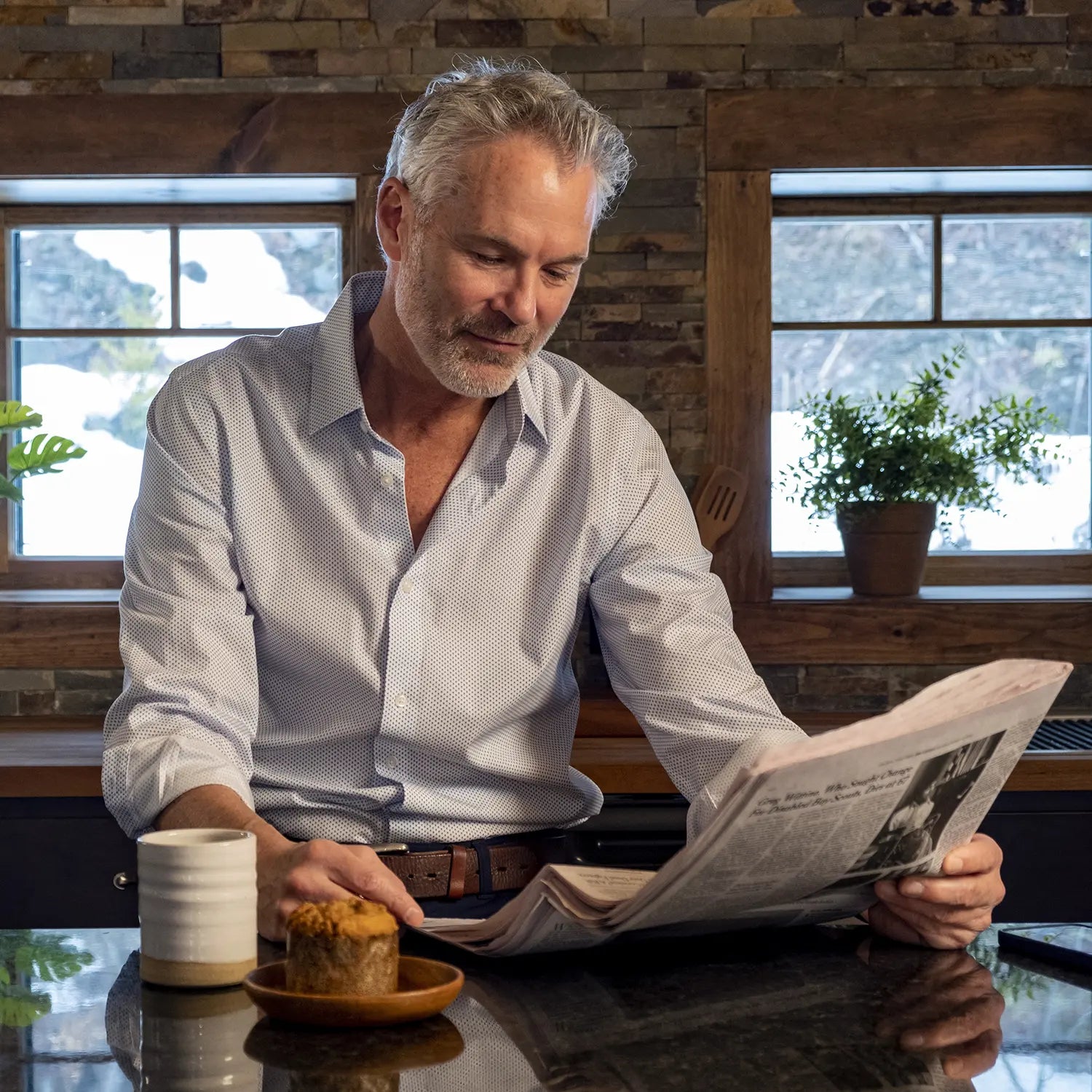 Male model sitting in the kitchen, reading the newspaper with a cup of coffee