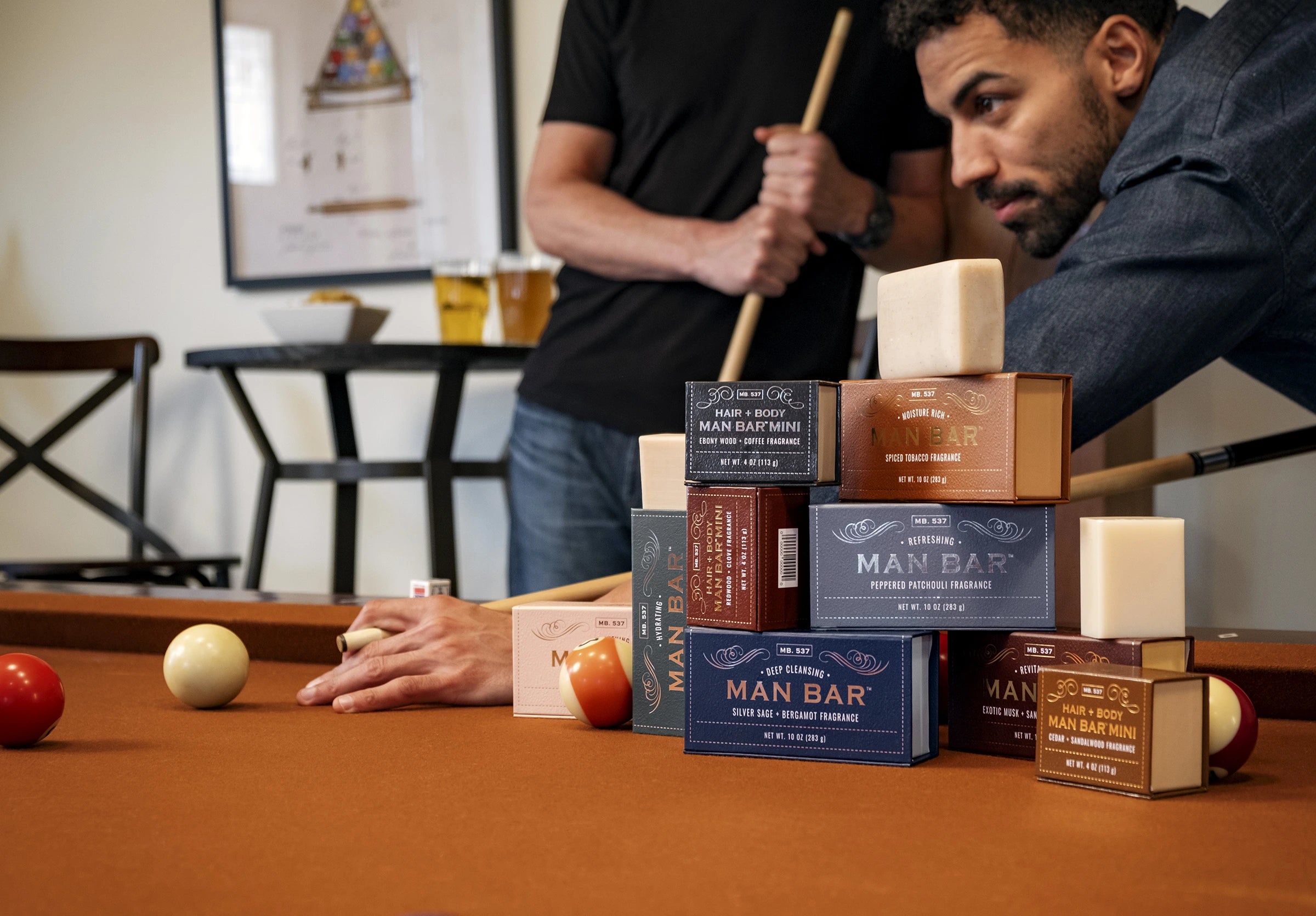An arrangement of Man Bar products stacked on a pool table with men playing billiards in the background